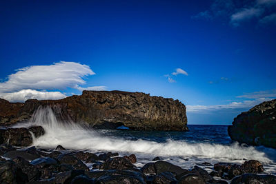 Sea waves splashing on rocks against blue sky