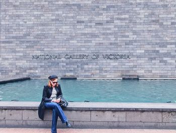 Full length of woman sitting against brick wall