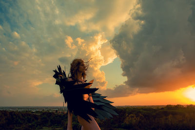 Woman standing on land against sky during sunset