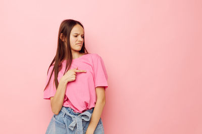 Portrait of young woman standing against pink background