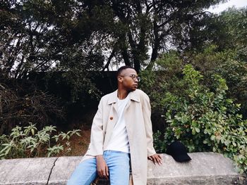 Young man sitting on ledge against trees