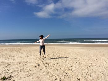 Full length of woman with arms outstretched walking on sand against sea at beach