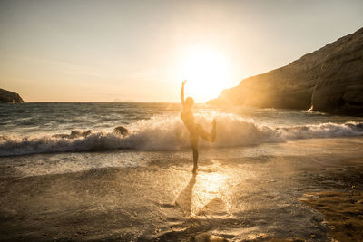 Silhouette of woman dancing on beach at sunset