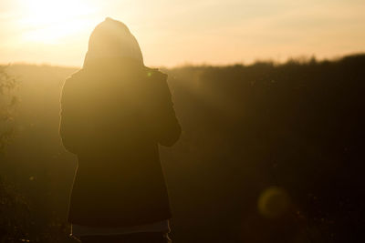 Rear view of woman standing against sky during sunset