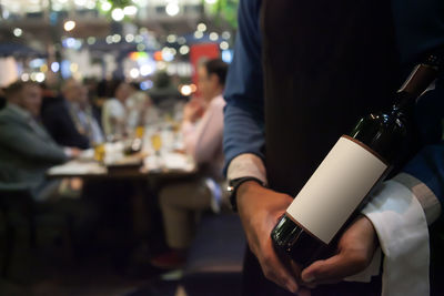 Midsection of waiter holding wine bottle at restaurant