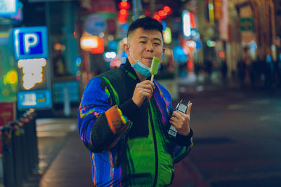 Portrait of young man standing against illuminated city at night