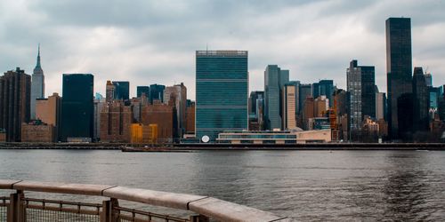 Modern buildings by river against sky in city