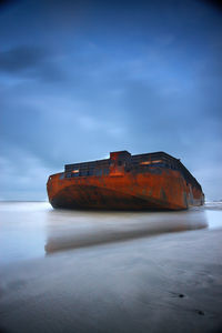 Abandoned ship on beach against sky