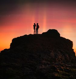 Silhouette man standing on rock against sky during sunset