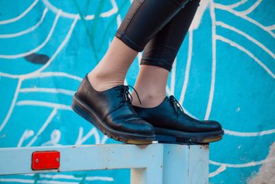 Low section of woman standing on metal against wall