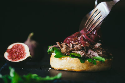 Close-up of hamburger with fig on table against black background