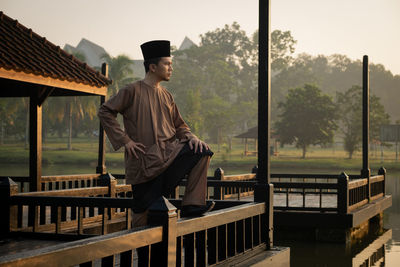 Man sitting on railing against trees