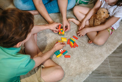 Unrecognizable mother and sons having fun playing wooden stacking piece game over carpet at home