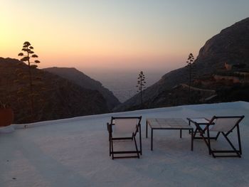 Empty deck chairs on mountain by sea during sunset