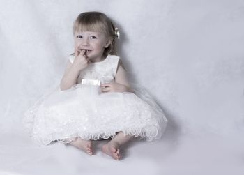 Portrait of cute little girl in white dress sitting on white background