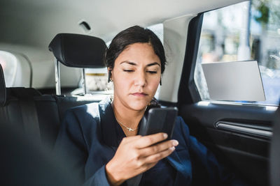 Businesswoman using smart phone while traveling in car