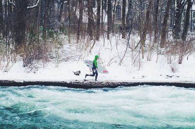 Full length of surfer running by river during winter