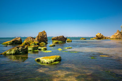 Rocks in sea against clear blue sky