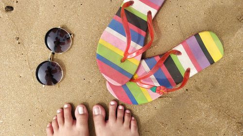 Low section of woman standing by flip-flops and sunglasses at beach