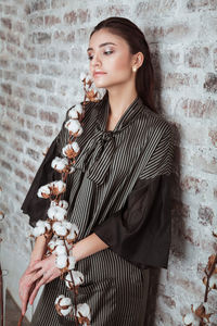 Thoughtful young woman with cotton plant standing against wall