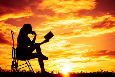 Silhouette woman sitting against orange sky during sunset