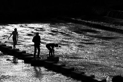 Silhouette people walking on stepping stones at kamo river