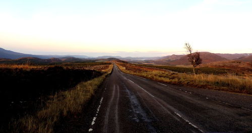 Empty road amidst landscape against sky