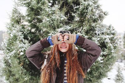 Woman in warm clothing covering eyes with hands against tree