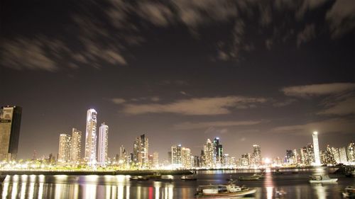 Illuminated city by sea against sky at night