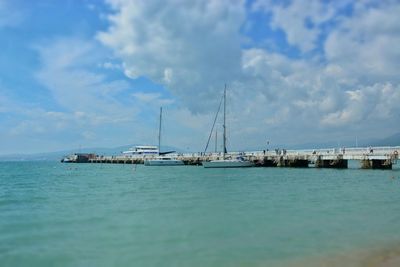 Boats in sea against cloudy sky