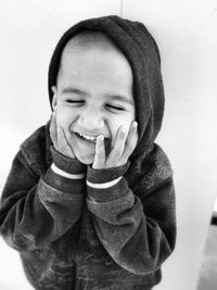 Smiling boy with hands on cheeks against wall