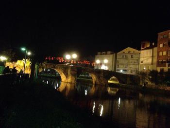 Illuminated bridge over river in city against sky at night