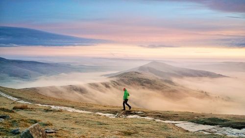 Side view of man walking on mountain against sky during sunset