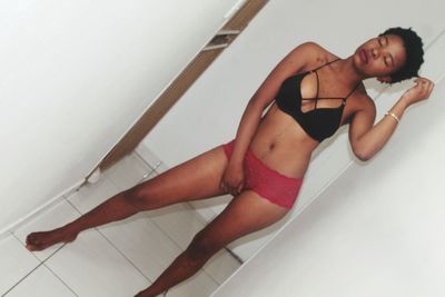 Young woman wearing bikini standing against wall in bathroom at home