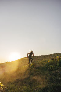 Woman exercising on hill against sky