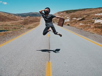 Rear view of man jumping on country road against sky