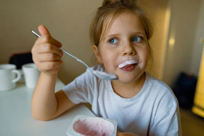 Cute girl eats yogur with appetite, has dirty mouth, has fun, grimaces