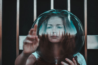 Close-up of young woman gesturing while wearing glass helmet in head against metallic railing