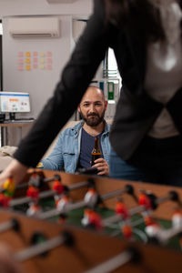 Smiling man watching colleague playing foosball