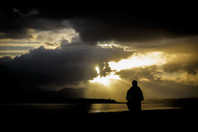 Silhouette man standing at beach against cloudy sky during sunset