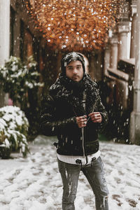 Portrait of man standing in snow against illuminated lighting equipment outdoors