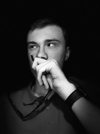 Young man holding sunglasses while standing against black background