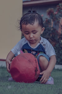 Cute baby girl holding old ball on grassy land