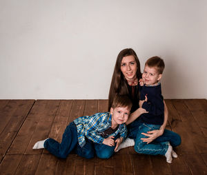Happy mom with two children, in casual clothes, are photographed sitting on the floor