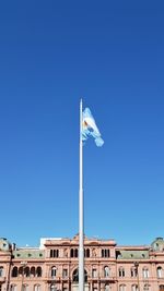 Low angle view of flag on building against clear blue sky