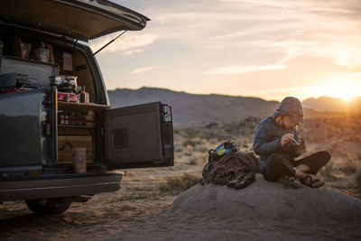 Woman eating food while sitting by van on field