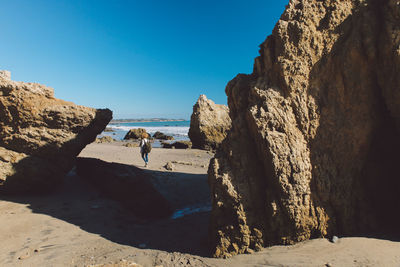 Mid distance view of mid adult woman by rock formations at beach