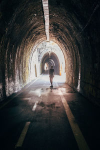 Rear view of silhouette woman skateboarding in tunnel