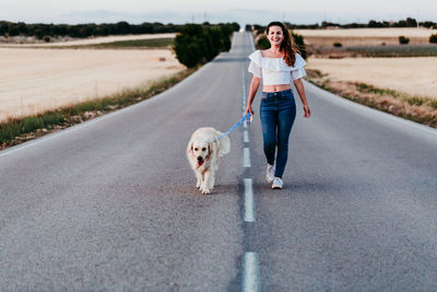 Woman walking with dog on road amidst field