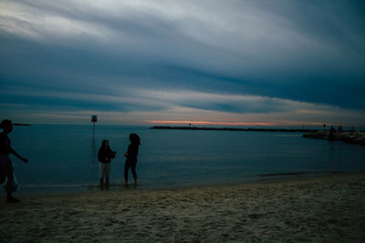 Silhouette people standing on beach against sky